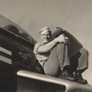 Original photograph of Wesley Chronister smiling in his sailor cap while seated on a jet early in his Navy career.